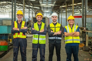 A group of four factory workers wearing hard hats and safety vests are posing for a photo in the factory.