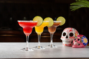 An array of margarita cocktails in different flavors, garnished with lime, beside vibrant sugar...