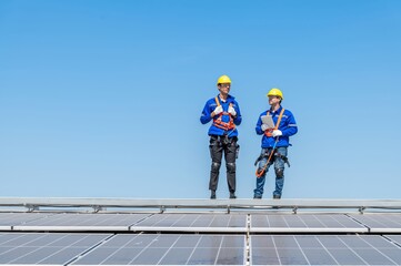 Two engineers in hard hats and safety gear inspect solar panels on a rooftop.