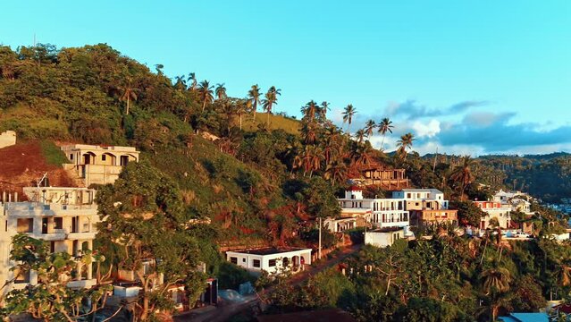 Summer landscape of an evening city on the mountain hills of the sea coast. Turquoise sky over the settlement. Tropical nature landscape. Orange reflections of the sun on the walls of houses.