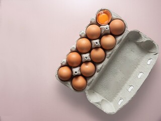 Open egg box with nine brown eggs and one broken egg showing yolk isolated. Fresh organic chicken eggs in carton pack. copy space - Powered by Adobe