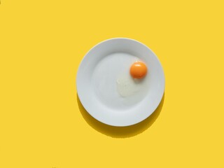 Raw egg on a white plate. View from above. Fresh egg with a bright yolk on a yellow background. - obrazy, fototapety, plakaty