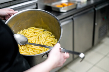 Person serving freshly cooked pasta from a large pot in a well-equipped kitchen, highlighting the readiness of a delicious meal