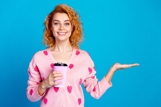 Photo of attractive young woman hold coffee paper cup palm empty space dressed stylish pink clothes isolated on blue color background