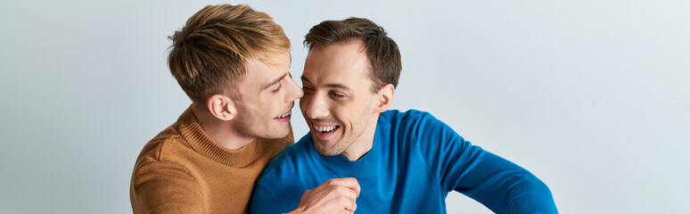 Obraz premium Two men, a loving gay couple, in casual attire, standing next to each other on a gray backdrop.