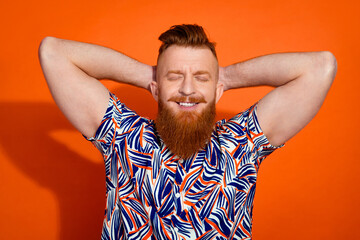 Photo of good mood dreamy guy dressed print shirt arms behind head closed eyes isolated orange color background
