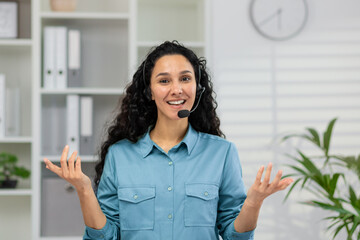 Enthusiastic young professional woman engaging in a video call, wearing a headset in a bright,...