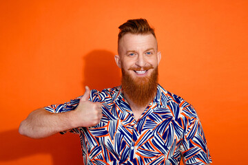 Photo of positive confident guy dressed print shirt showing thumb up isolated orange color background