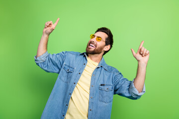 Photo of cheerful cool guy wear denim jacket having fun pointing two fingers empty space isolated green color background