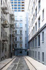 Backyard in downtown San Francisco (USA). Facades, balconies, windows, floor and walls of city houses in shades of grey, white and pale blue. Dead end small road with vanishing point perspective.