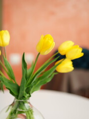Obraz premium Bouquet of yellow tulips in a transparent glass vase stand on a white table