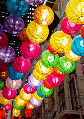 Chinese lanterns in Chinatown San Francisco, (USA). Green, turquoise, yellow, red, blue and orange spherical lamps, backlit by sun hanging as decoration above a downtown shopping street.