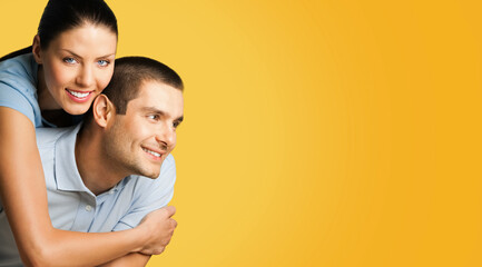 Portrait of standing close embracing couple in blue casual clothing, love studio concept, isolated over yellow background. Young brunette man and woman posing together.  Wide banner image