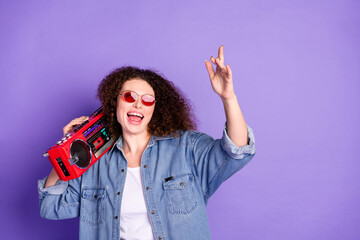 Portrait of pretty young woman carry boombox empty space wear denim shirt isolated on purple color...