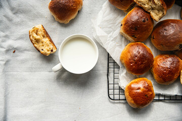 Freshly baked aromatic homemade chocolate and lemon brioche buns on cooling rack and cup of milk on linen tablecloth.