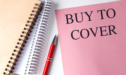BUY TO COVER text on pink paper with notebooks