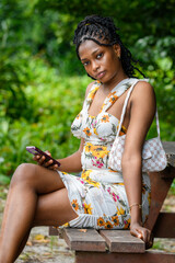 A young african lady using her phone while seated at a park bench