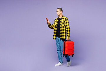 Traveler man he wear yellow casual clothes hold bag use mobile cell phone isolated on plain purple...