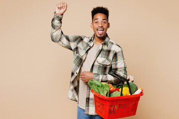 Young smiling happy fun man he wears grey shirt hold red basket bag with food products doing winner...
