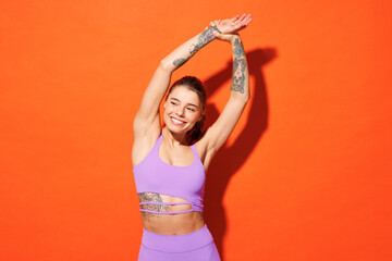 Young fitness trainer sporty woman sportsman wearing purple top clothes spend time in home gym doing stretch exercise rising hands up isolated on plain orange background Workout sport fit abs concept