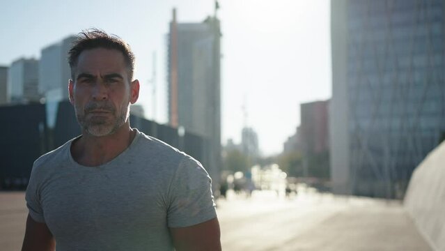 Strong mature man warming up doing sprints ready to go for a run. Middle aged man training looking seriously at the camera. People doing cardio daily sports routine in urban area outdoor