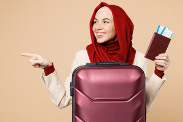 Traveler Asian Muslim woman wear red abaya hijab hold passport ticket bag point aside isolated on...