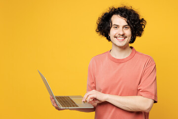 Young smiling fun happy IT man he wear pink t-shirt casual clothes hold use work on laptop pc...