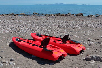 Recreational red kayak with paddles and hard plastic seat back, on the beach