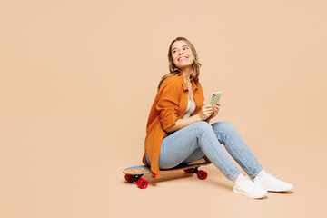 Full body young woman she wear orange shirt casual clothes sits on pennyboard skateboard hold in...