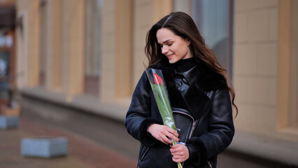Portrait of a happy brunette girl with a tulip in the background of the city in the cold season.