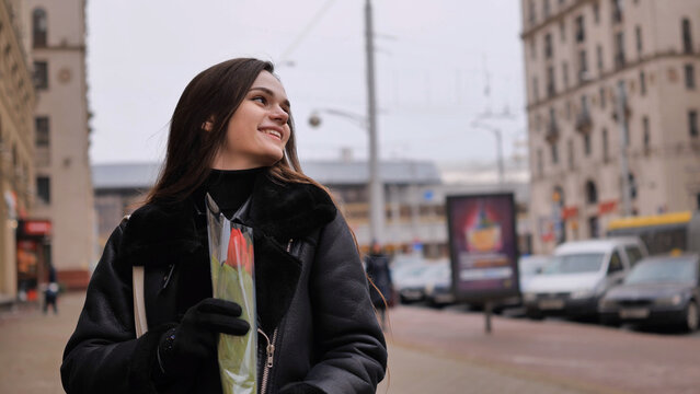 Portrait of a happy brunette girl with a tulip in the background of the city in the cold season.