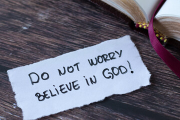 Do not worry, believe in God, handwritten quote on paper note with open holy bible book on wooden...