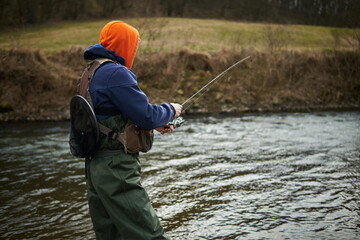 Fisherman fishing by the river in daytime with tackle bag and net