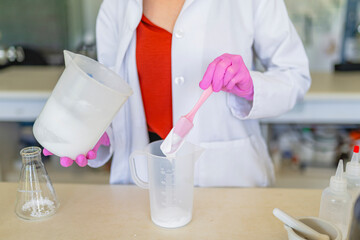 Crop female chemist putting chemical liquid in test jar at laboratory