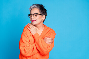 Photo portrait of lovely senior lady hugging self dressed stylish orange garment isolated on blue color background