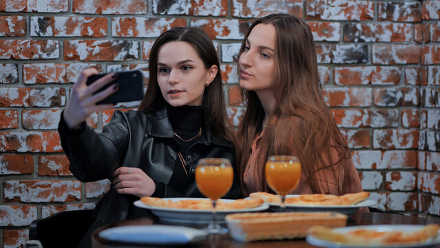 Two beautiful stylish young girls have lunch in a cafe and take a selfie