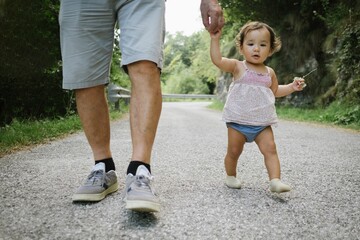 baby girl walking together with her grandfather during a stroll in a park. Concept of grandpa and...