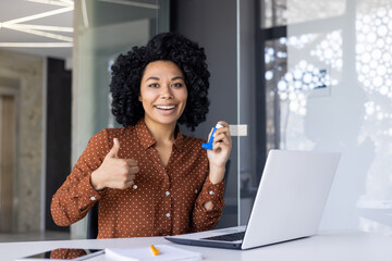 A cheerful young African American woman gives a thumbs up at her office desk after using her asthma...