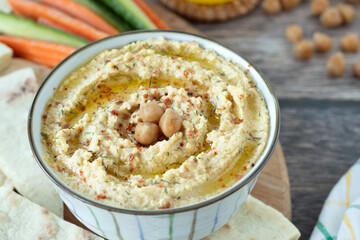 Traditional chickpea hummus with olive oil and herbs in bowl with pita bread and vegetable sticks...