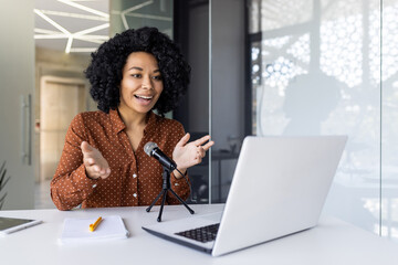 A cheerful young African American woman recording a podcast in a well-lit modern office setting....