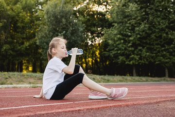 Photo of child girl drinking water after running. Healthy active lifestyle concept.