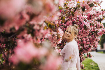 Smiling young woman surrounded by pink spring blossoms. Concept of self-care, new beginning