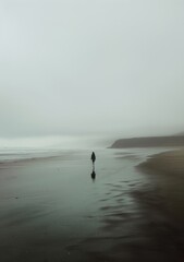 Person Walking Across Sandy Beach on Foggy Day