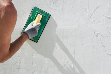 Close-up of construction worker's hands plastering and smoothing wall. Concept of house renovation.