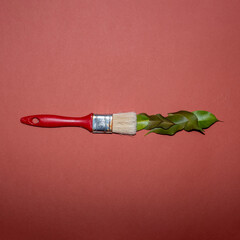 Fototapeta premium Red paintbrush and green leaves creative flat lay concept on an orange background.