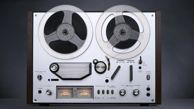 Old steel reel-to-reel tape recorder plays on a dark background in 4K. Front view