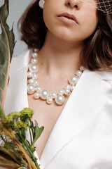 A woman wearing a white blazer and a pearl necklace is posing for a photo. The necklace is made of...