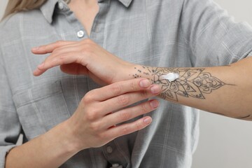 Obraz premium Tattooed woman applying cream onto her hand on light background, closeup