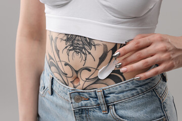 Woman applying healing cream onto her tattoos against grey background, closeup - obrazy, fototapety, plakaty