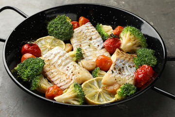 Tasty cod cooked with vegetables in frying pan on grey table